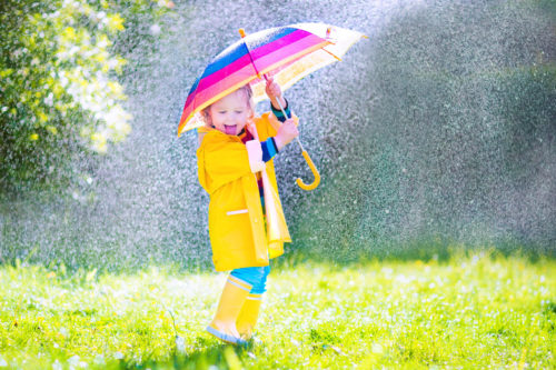 Funny little toddler with umbrella playing in the rain